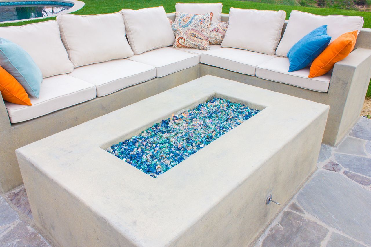 Outdoor concrete sectional sofa with blue and orange pillows, and fire pit with blue glass.
