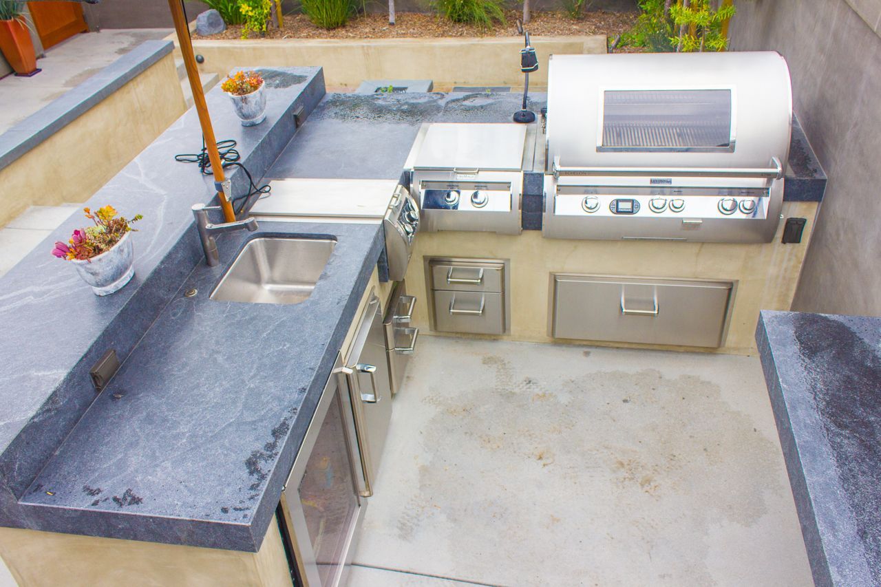 Outdoor kitchen with granite countertops, stainless steel appliances, sink, and grill.