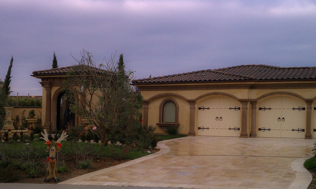 Tan stucco house with arched garage doors, driveway, and cloudy sky.
