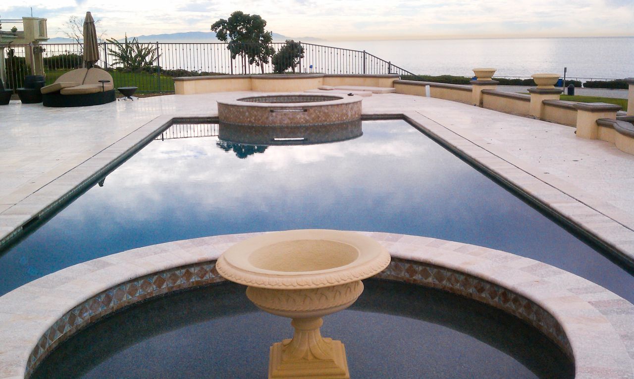 Pool with water features, ocean view, and light-colored stone patio.