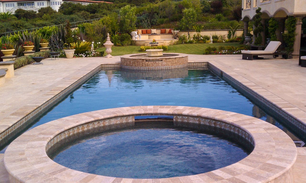 Swimming pool with jacuzzi and fountain, surrounded by patio and landscaped yard.