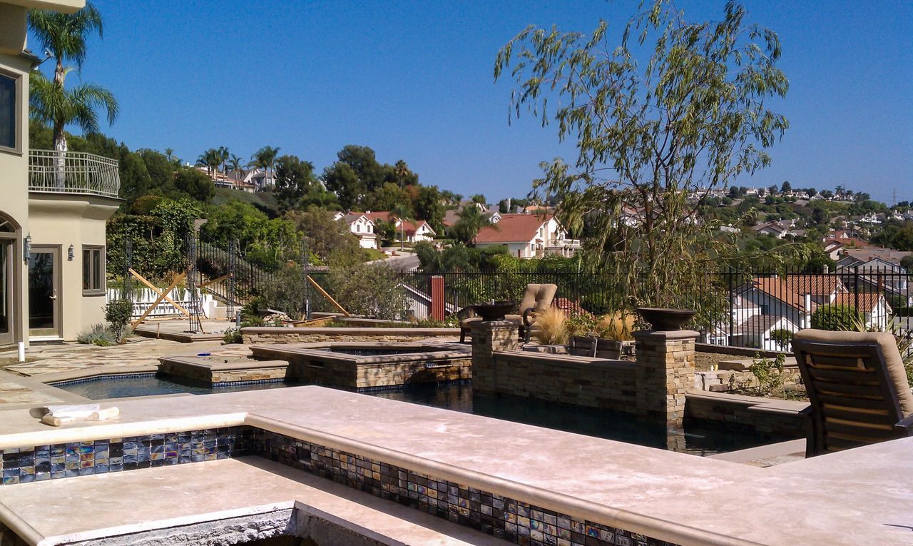Outdoor patio with a pool, overlooking a neighborhood with homes under a blue sky.