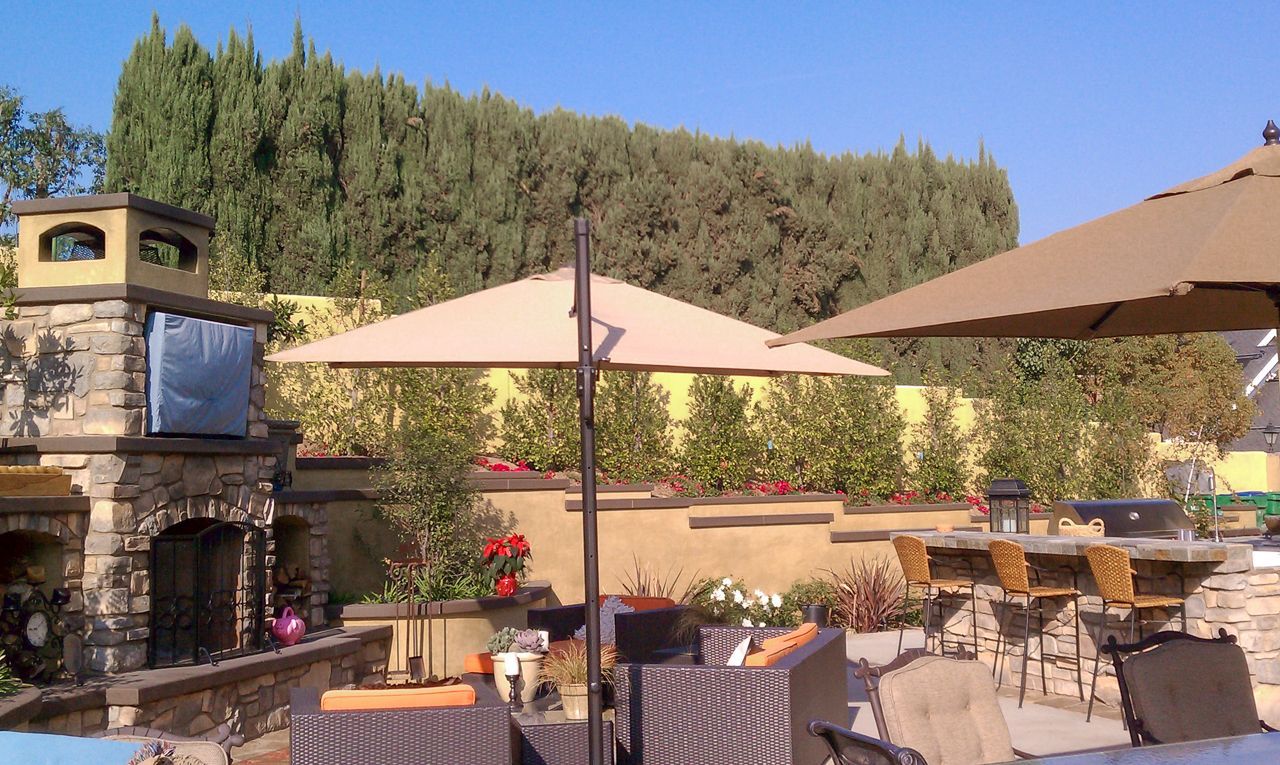 Outdoor patio with a stone fireplace, umbrellas, and bar seating.