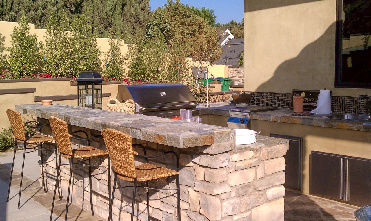 Outdoor kitchen with stone bar, grill, and seating.