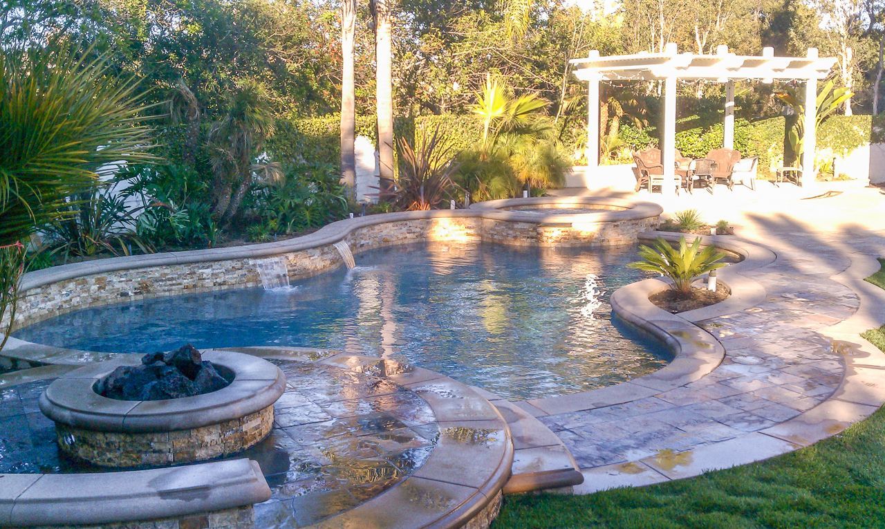 Pool with stone features, a fire pit, and a pergola in a backyard setting.