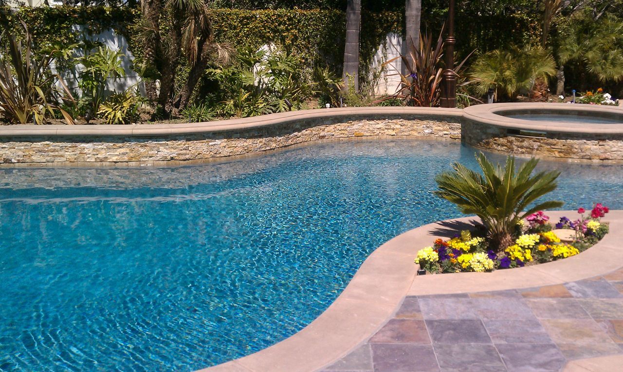 Blue swimming pool with stone border and island of flowers.