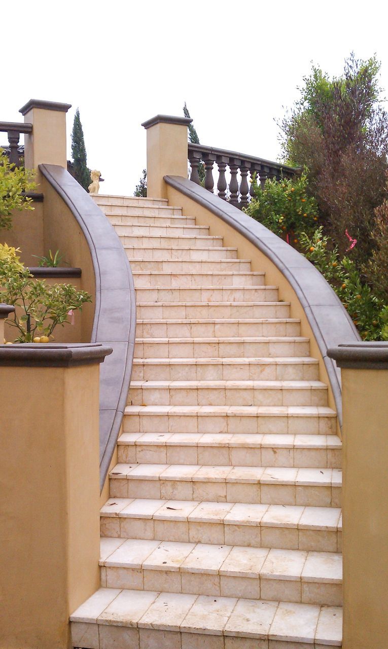Stone staircase curves upward, flanked by beige walls and a wrought-iron balustrade.