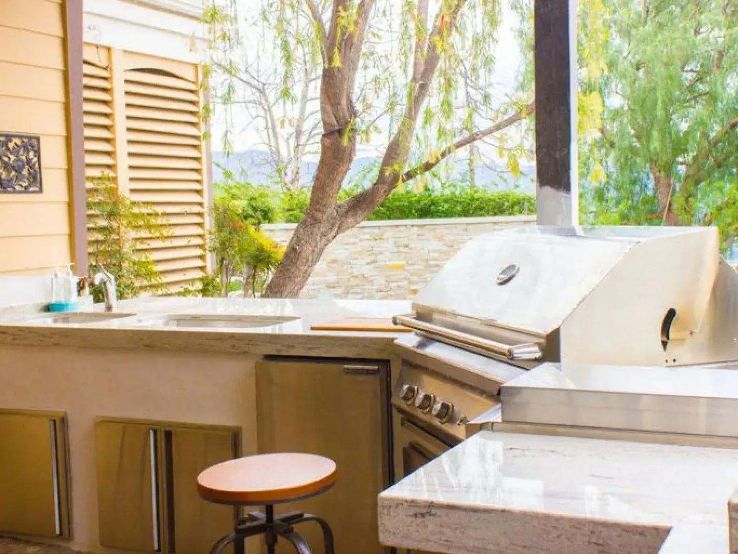 Outdoor kitchen with grill, sink, and prep area, overlooking a landscape.
