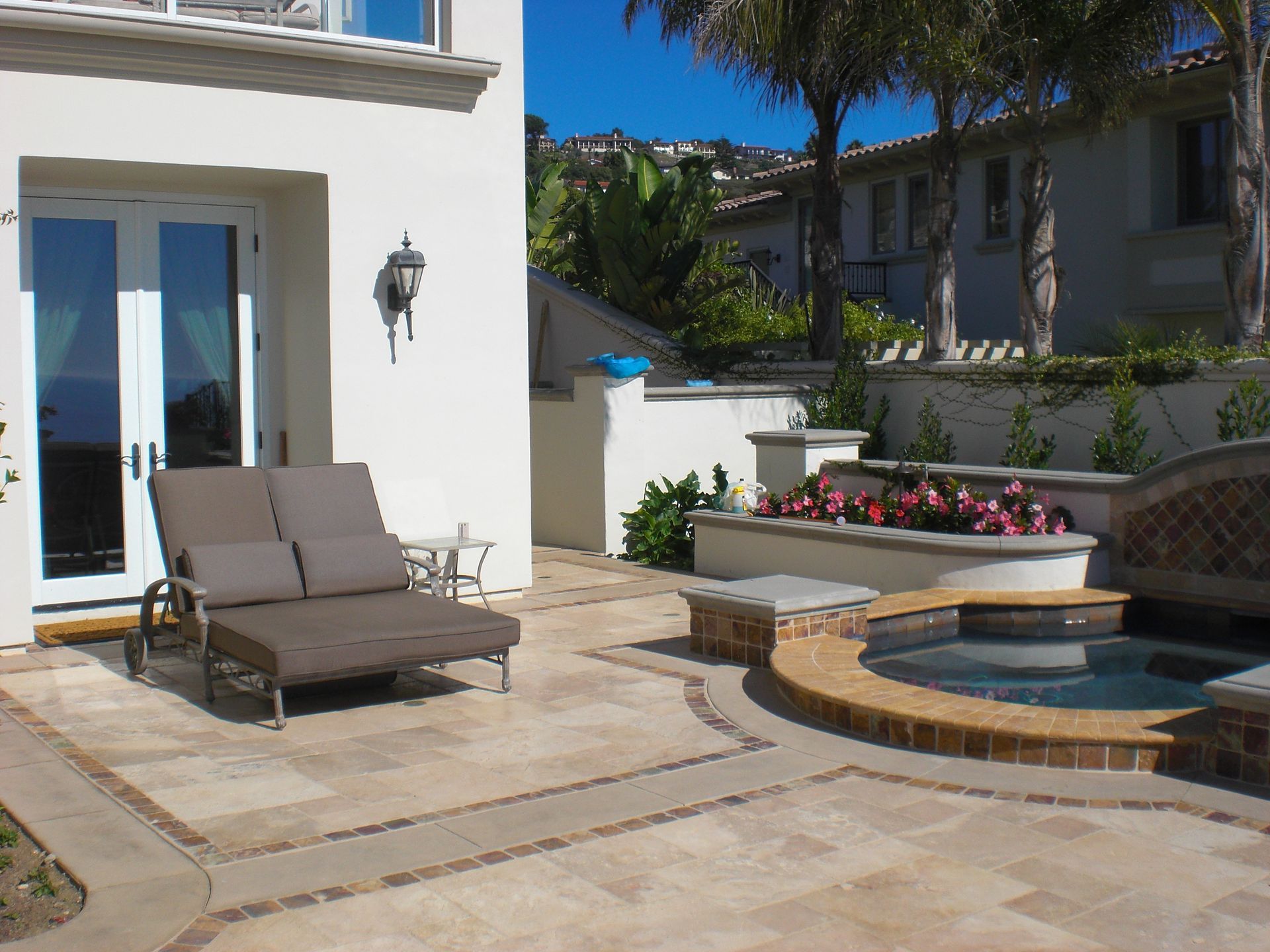 Patio with a lounge chair, jacuzzi, and landscaping; bright sunny day.