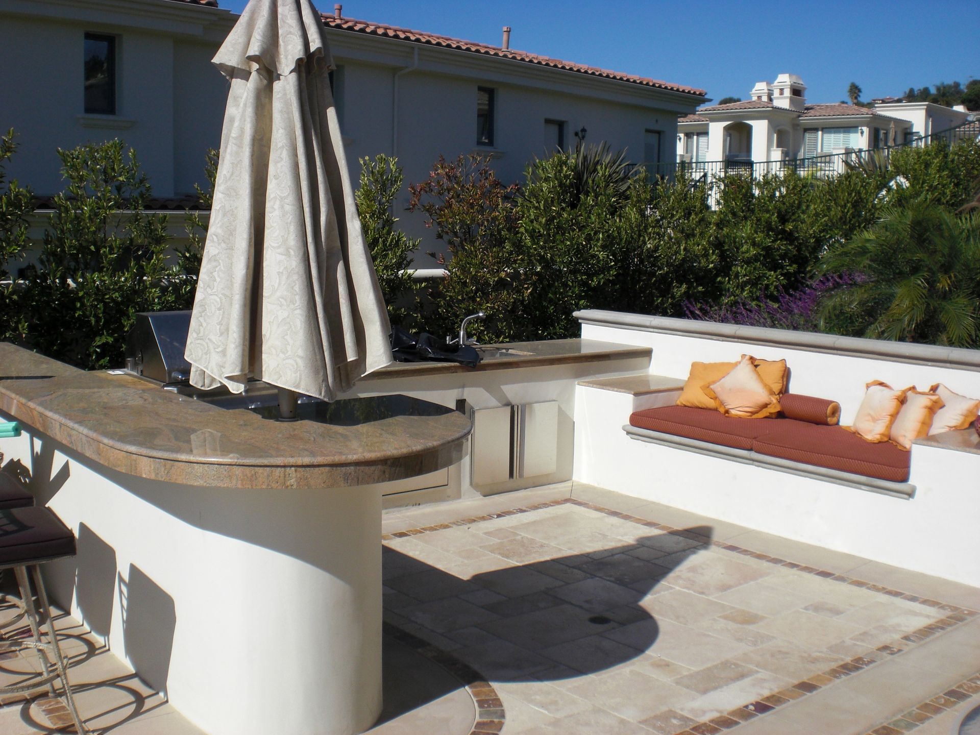 Outdoor patio with bar, built-in seating, umbrella, and view of houses.