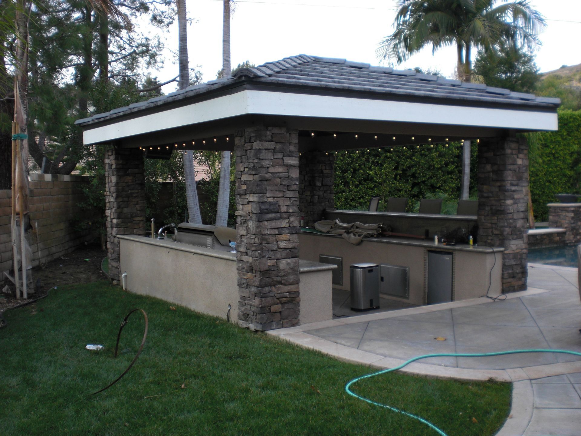 Outdoor kitchen with stone pillars, countertop, and appliances under a roof.