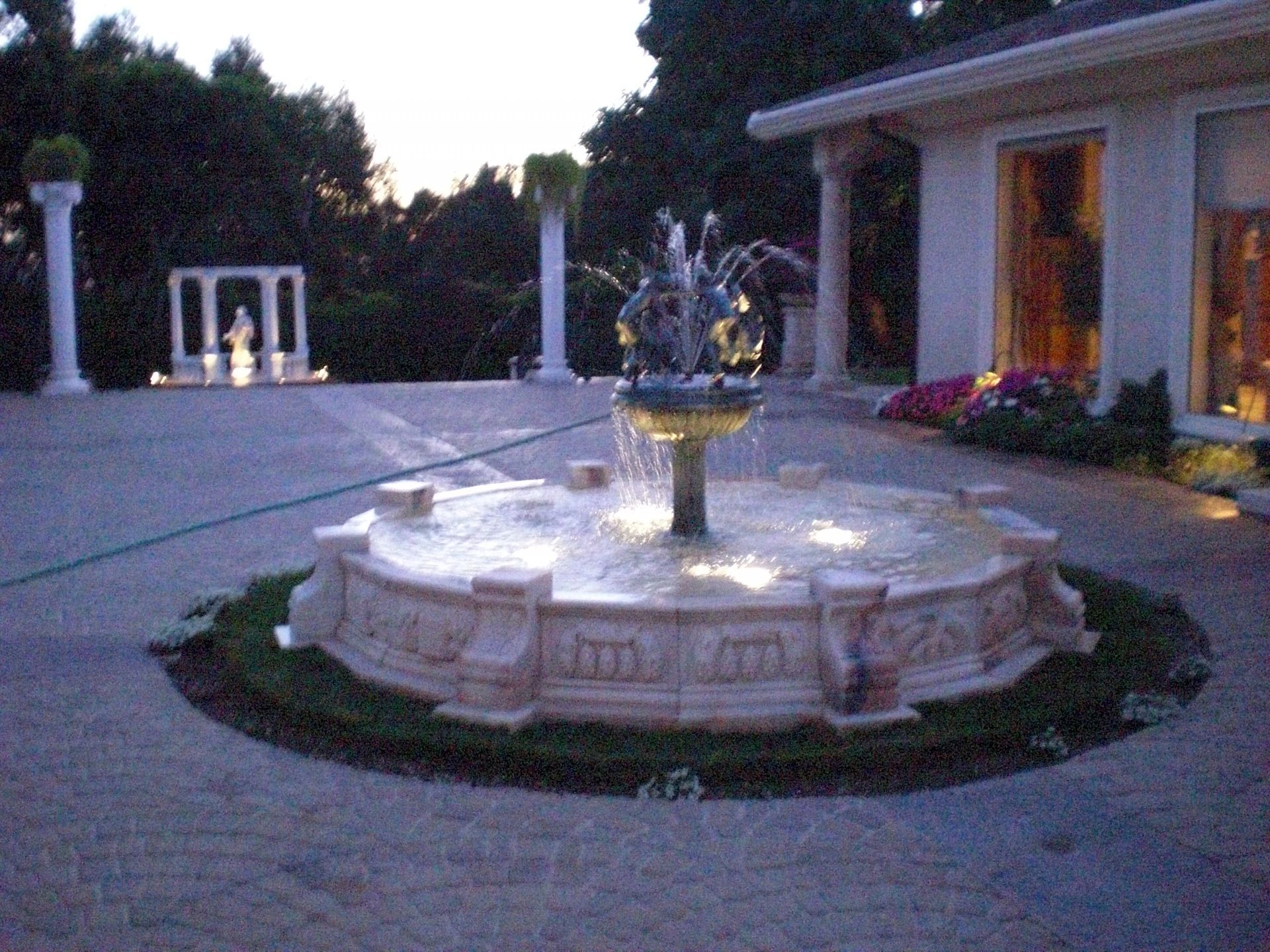 Fountain with bronze sculptures sprays water into a large circular pool, front of a building.