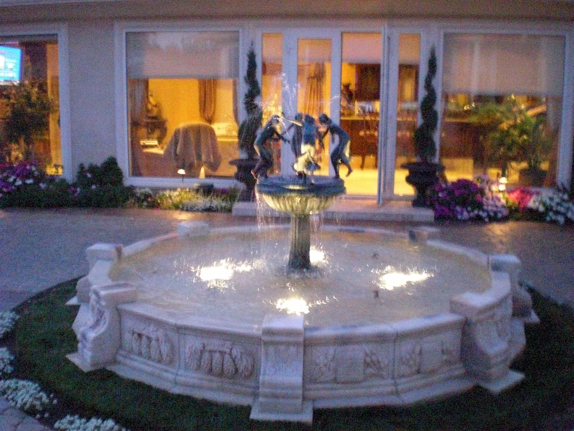 Fountain in front of a house, with water features, statues, and surrounding flowers.