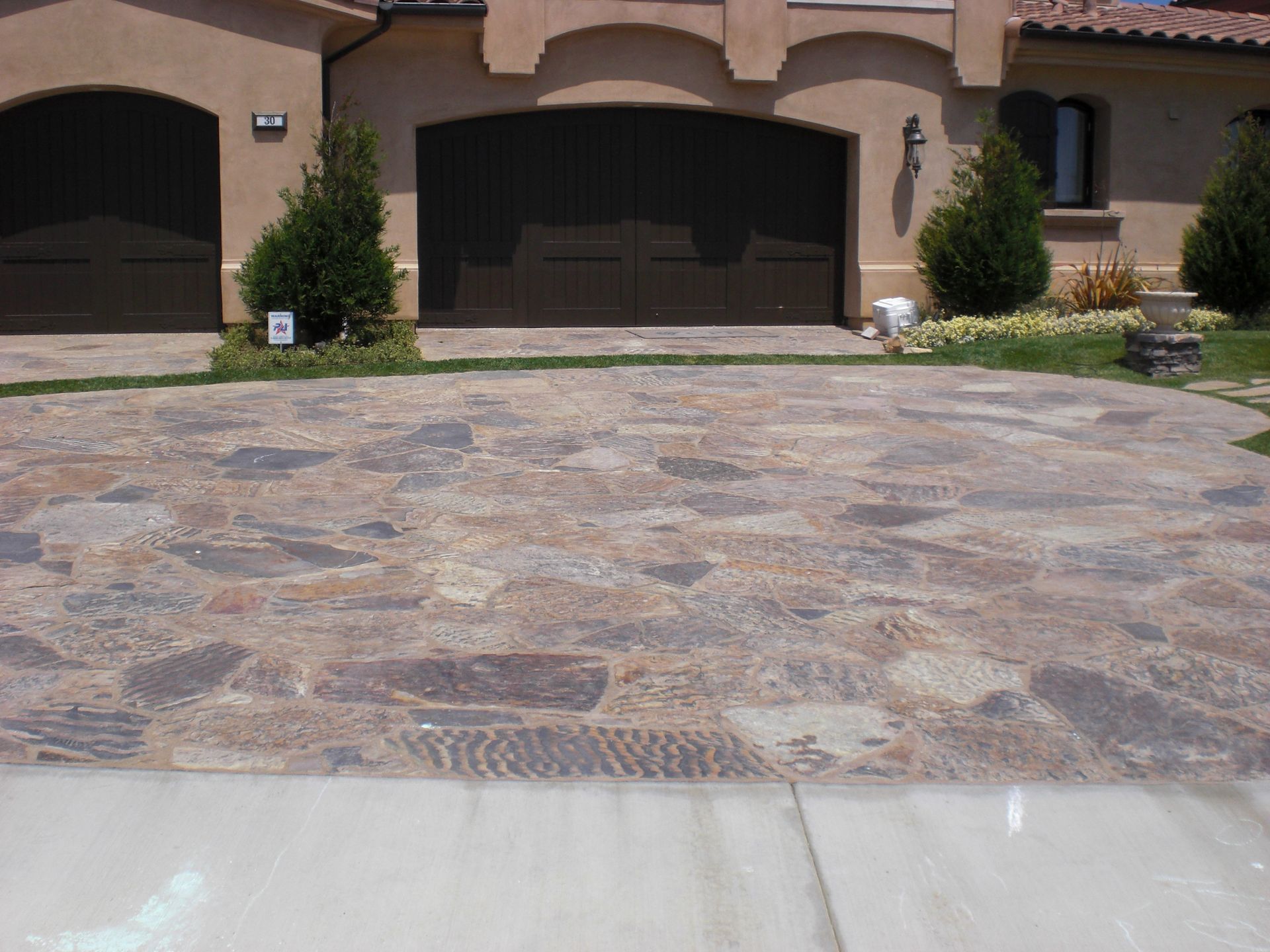 Driveway paved with multicolored stone leading to a house with a brown garage door.