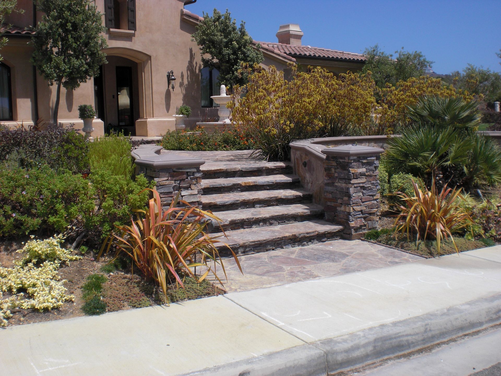 Stone steps leading up to a beige house, surrounded by landscaping and sidewalk.