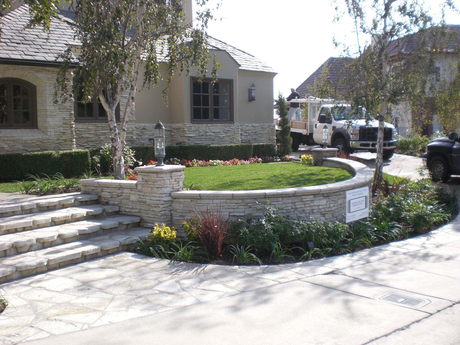 Stone steps lead to a landscaped yard with a curved retaining wall. A truck is parked in the driveway.