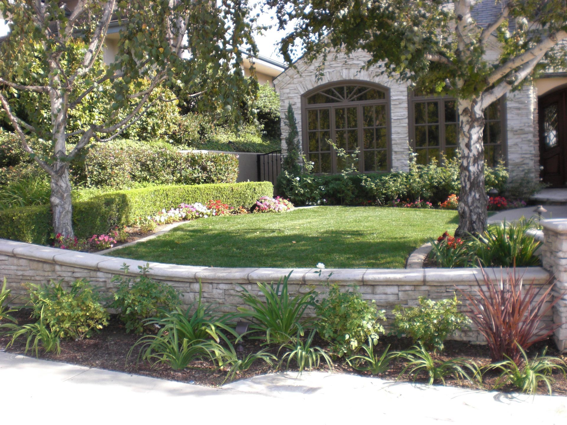Stone house with manicured lawn, shrubs, and flower beds. Sunny outdoor setting.