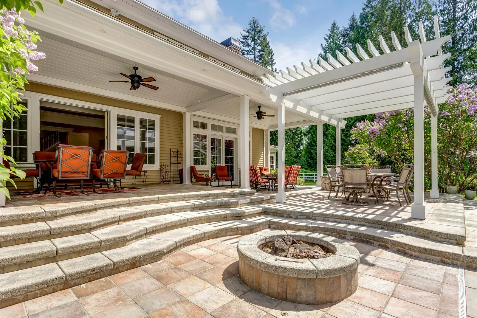 Patio with fire pit, pergola, and seating near a house with French doors.