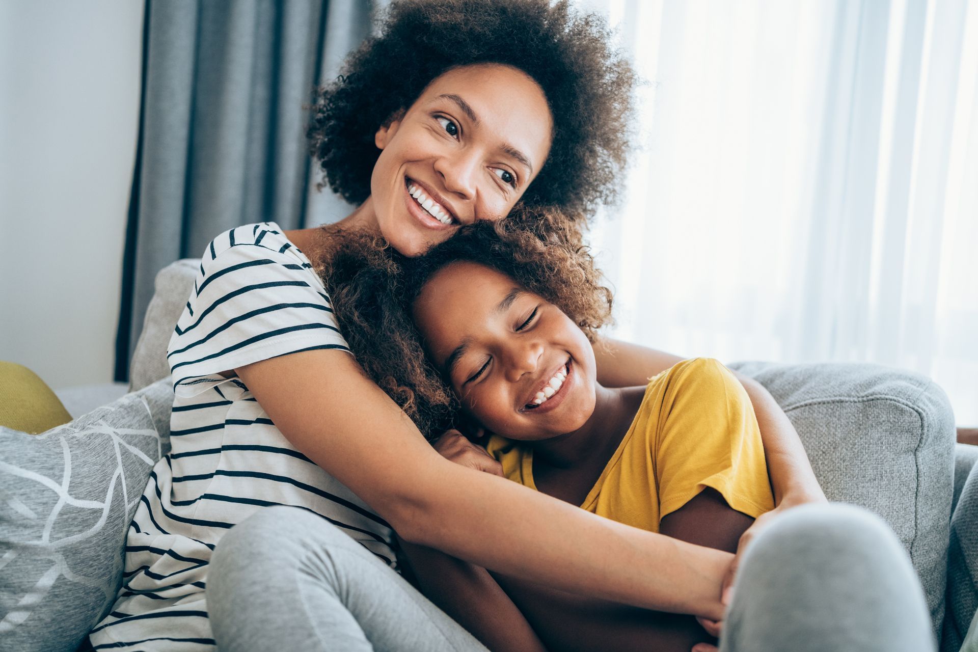 A mother and daughter are hugging each other on a couch.