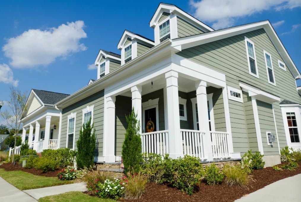 Green house with white trim and porch columns under a blue sky
