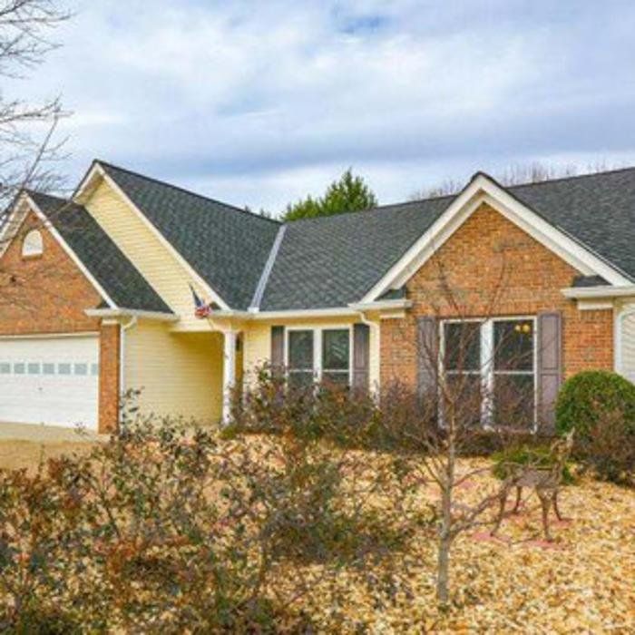 Suburban brick house with gray roof, white garage, and leaf-covered front yard