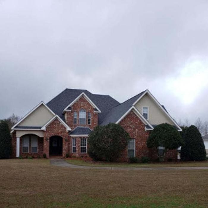 Large brick suburban house with a dark roof and front lawn under a cloudy sky