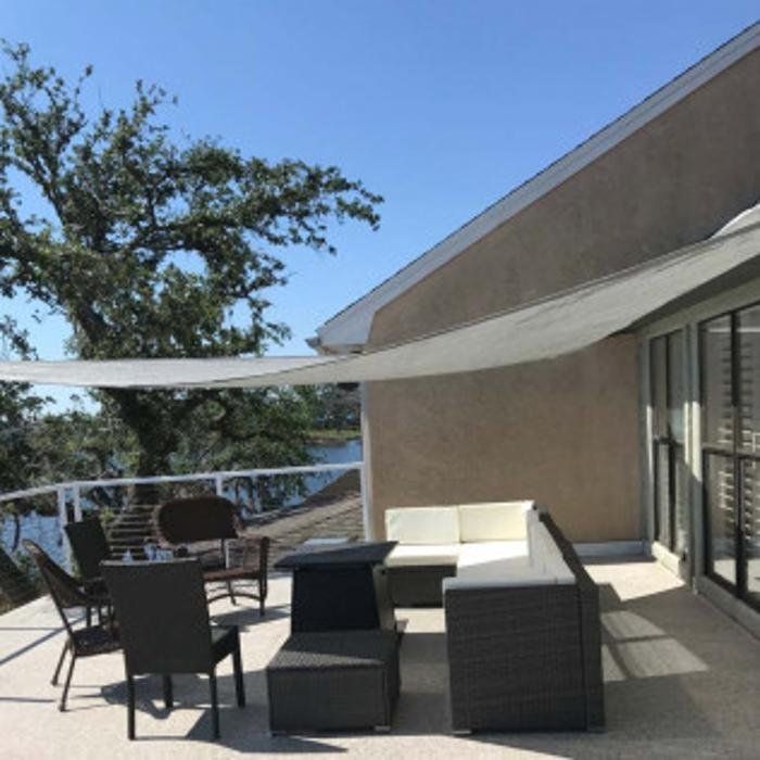 Patio with wicker chairs and table under a shade sail beside a house and sliding glass doors