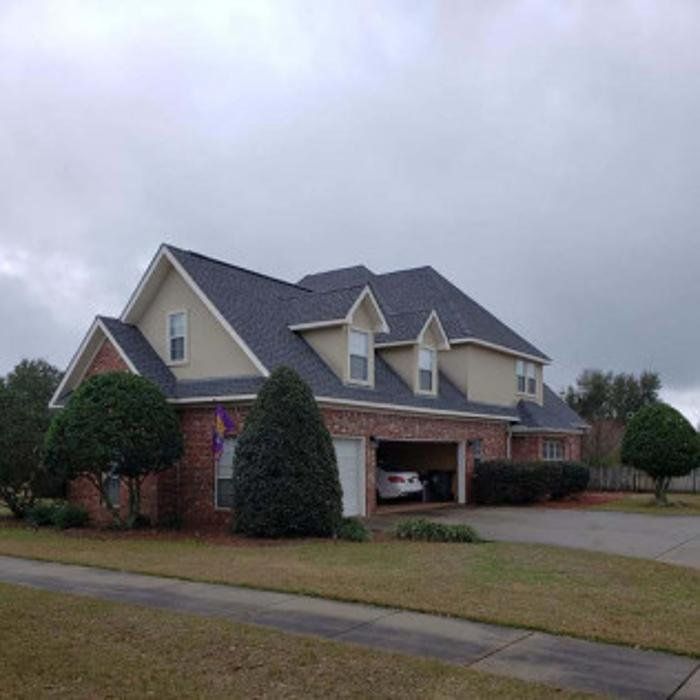 Suburban house with beige siding, brick lower level, and a two-car garage under a cloudy sky