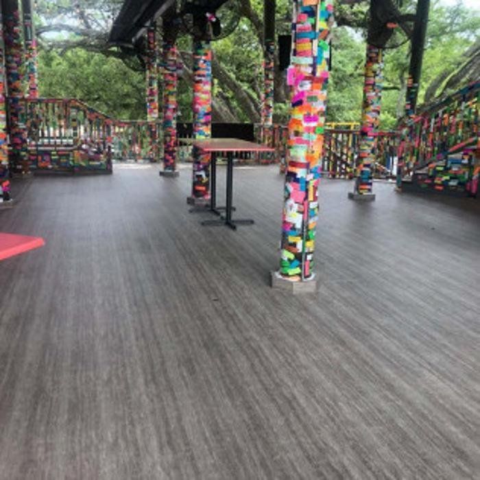 Colorful outdoor pavilion with ribbon-covered pillars, wooden floor, and surrounding trees