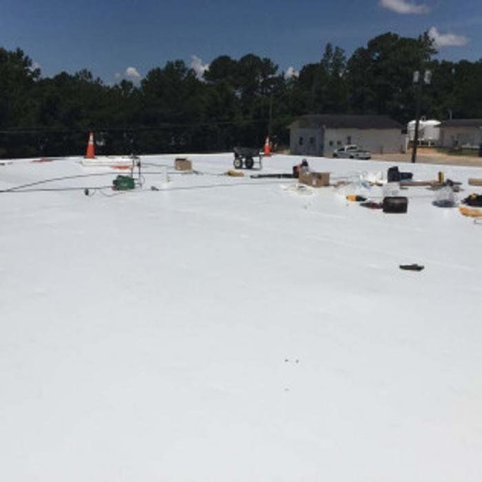 Flat white rooftop with scattered tools and materials near trees and a small building under a blue sky