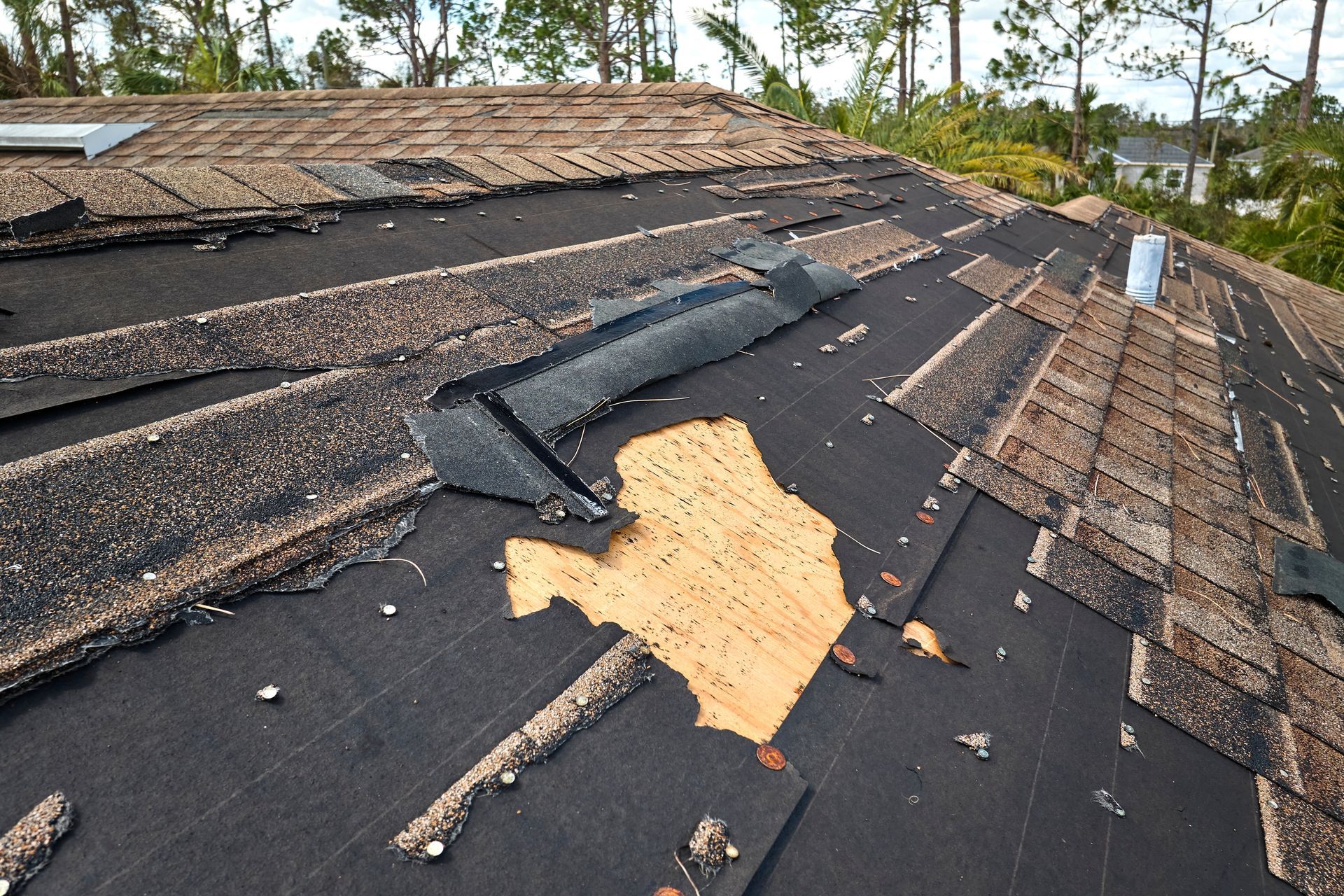 Damaged shingle roof with missing sections and exposed underlayment after storm damage