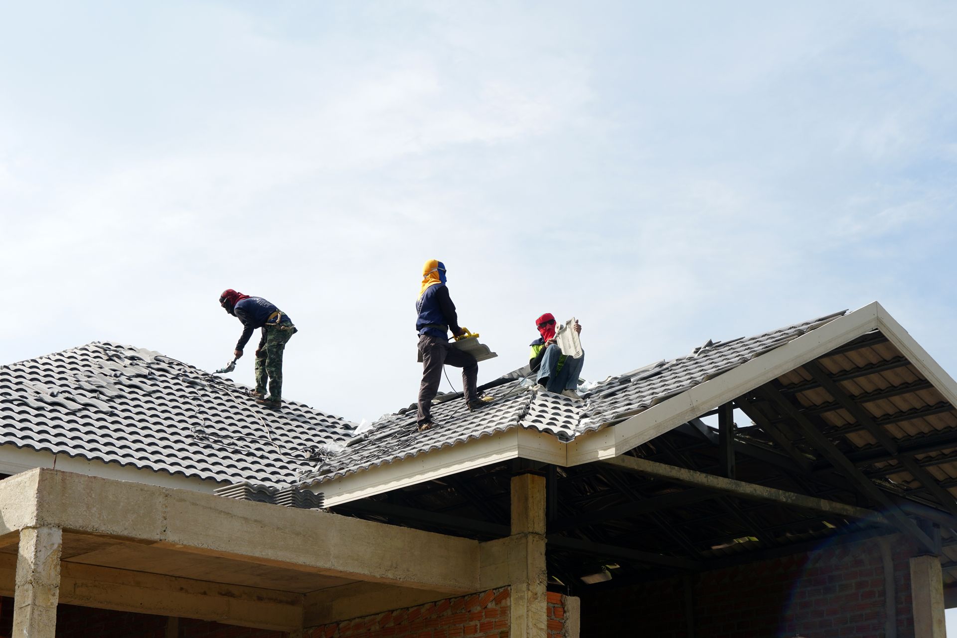 Three workers on a roof installing shingles on a house under construction