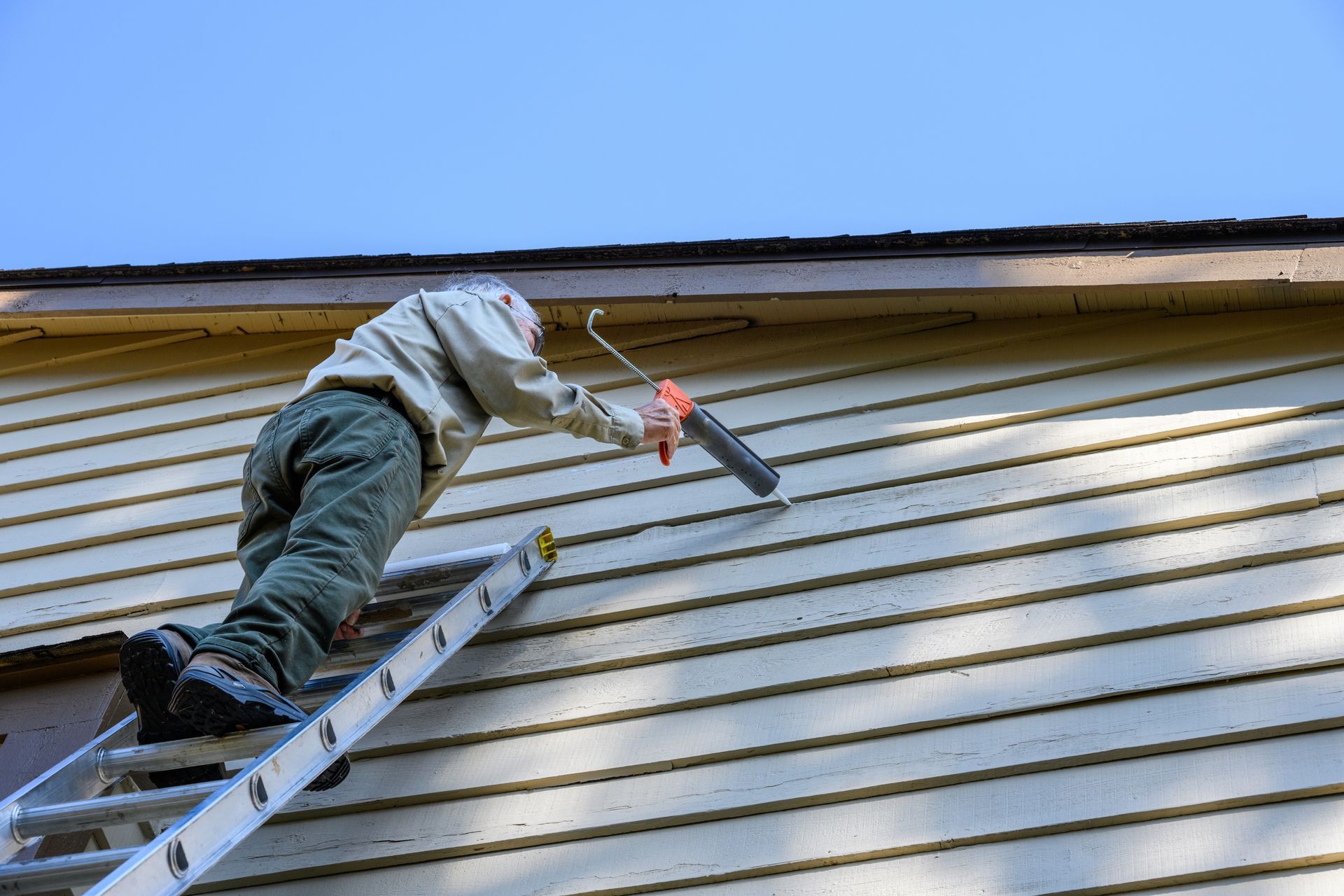 Worker on a ladder painting the side of a house with a roller