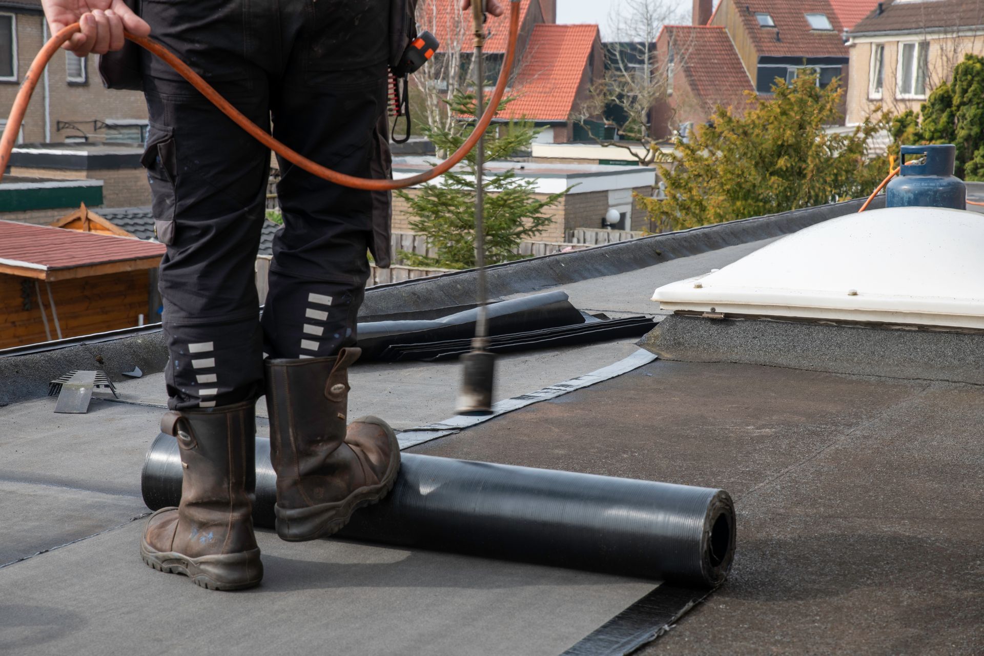 Worker installing black roofing material on a flat roof with buildings in the background