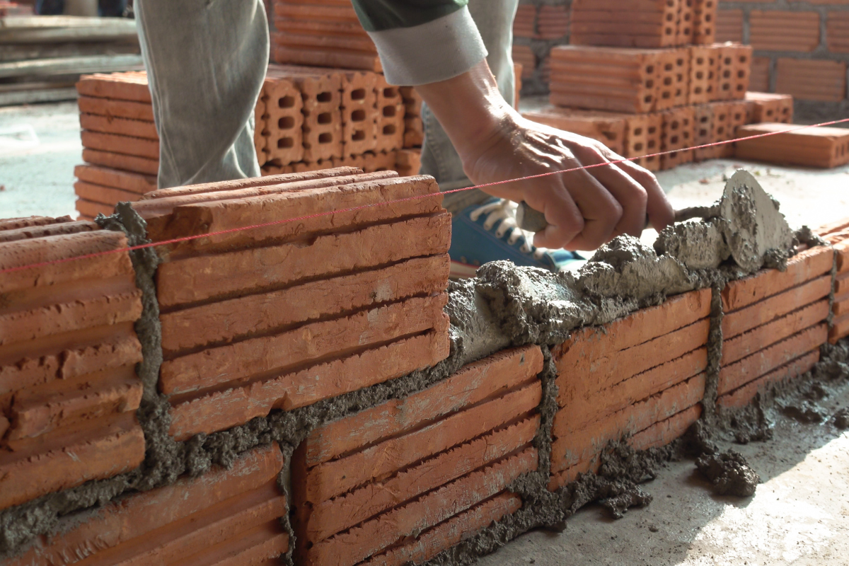 Worker laying mortar between red bricks on a construction wall