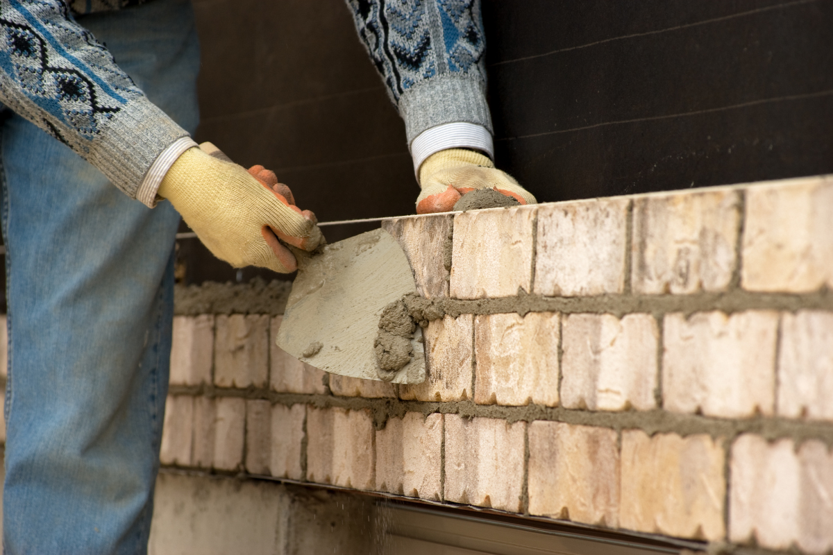 Worker spreading wet mortar on a brick wall with a trowel