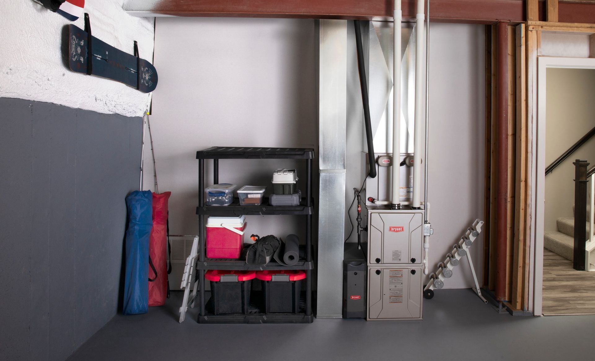 Basement interior with furnace, storage shelves, and ductwork. Gray walls and flooring.