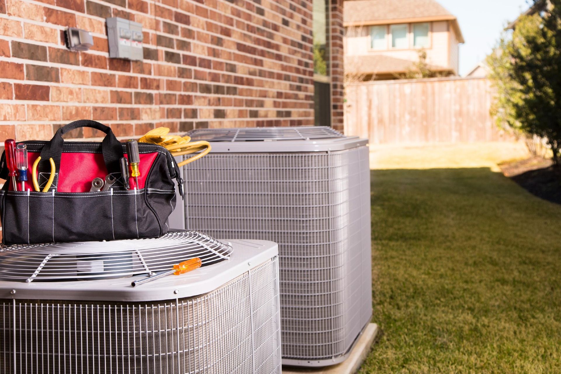 HVAC unit with toolbox, set against a brick wall and a grassy backyard.