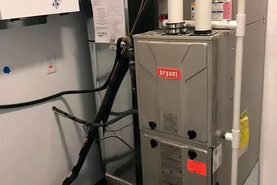 A Bryant furnace in a utility room with pipes and wiring.