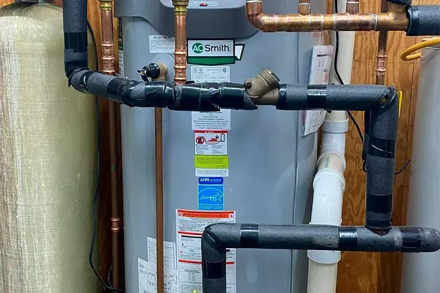 Hot water heater with insulated pipes and copper plumbing in a utility room.