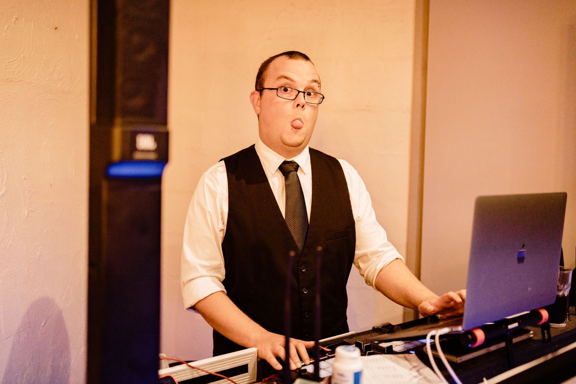 A man in a vest and tie is playing music on a laptop.