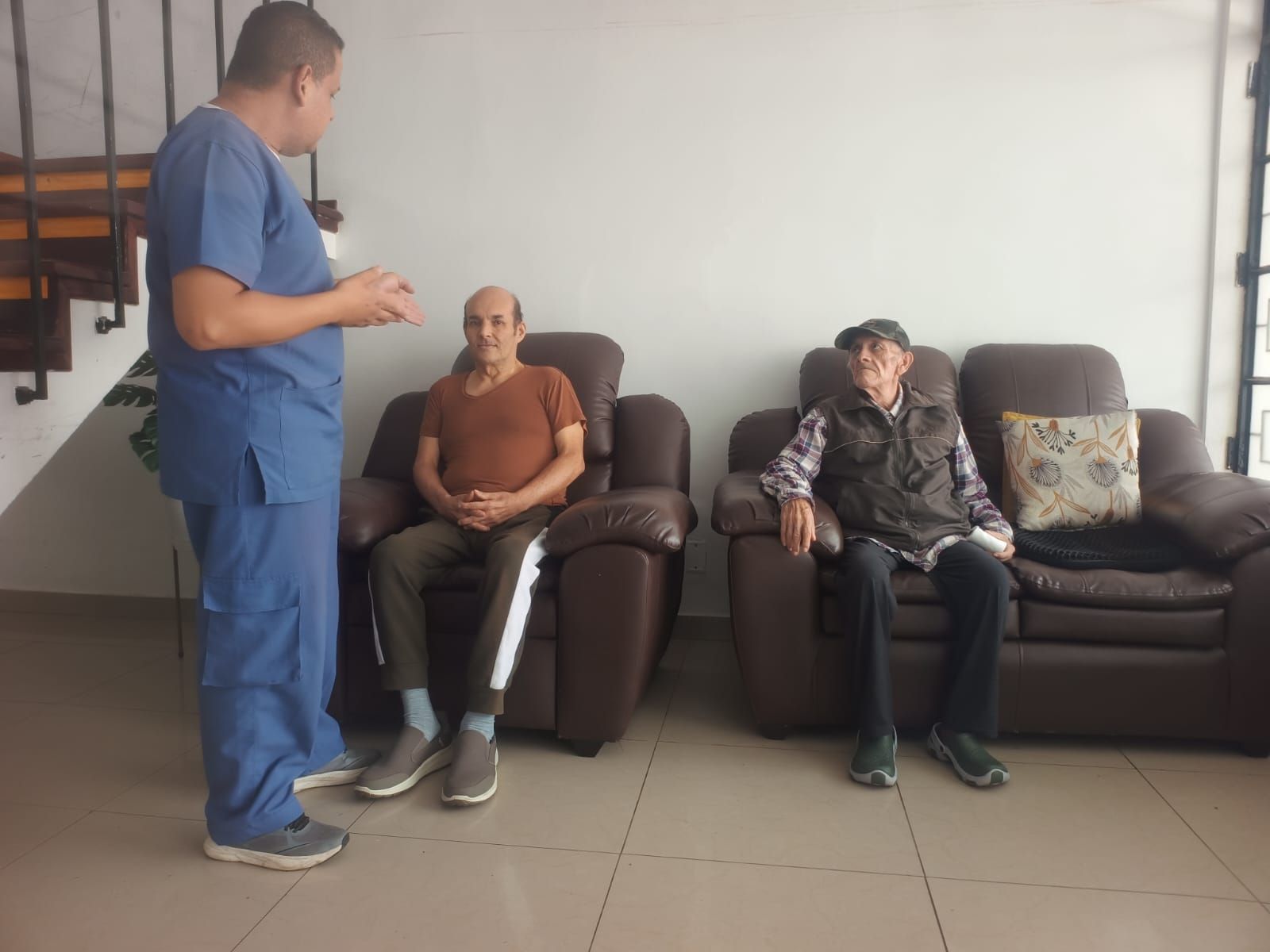 Dos personas están sentadas en un banco en una habitación luminosa, sonriendo y tomadas de la mano 