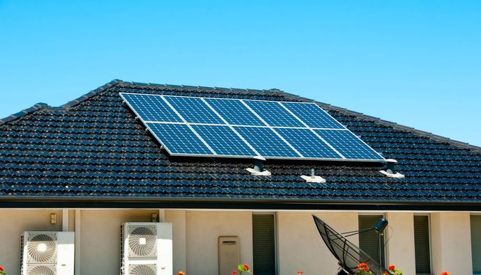 A person installing a solar panel on a gray corrugated metal roof.