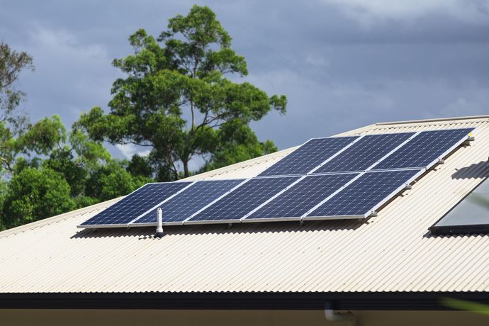 A person installing a solar panel on a gray corrugated metal roof.