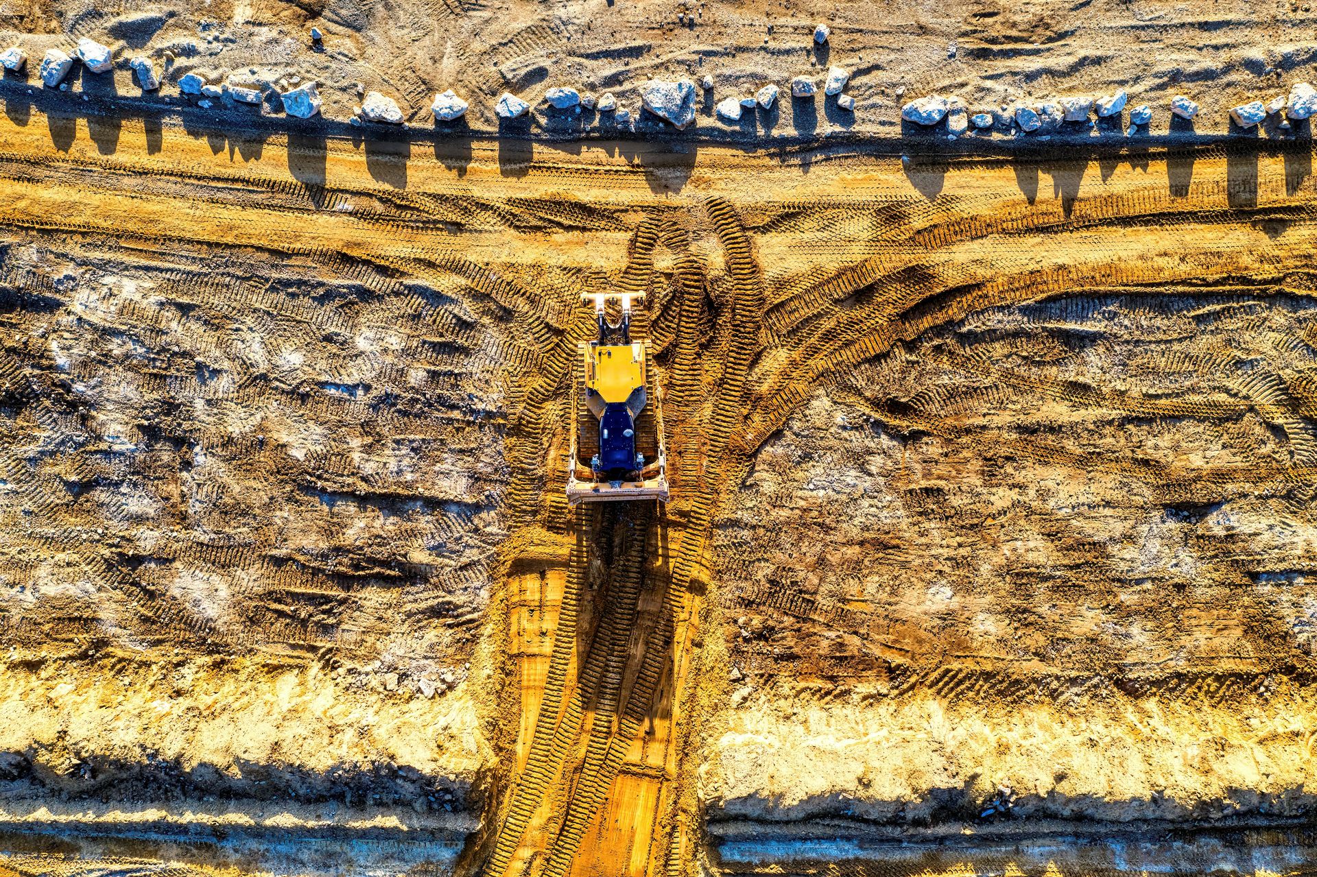 Bulldozer cutting a dirt path through a quarry wall, with workers along the top edge