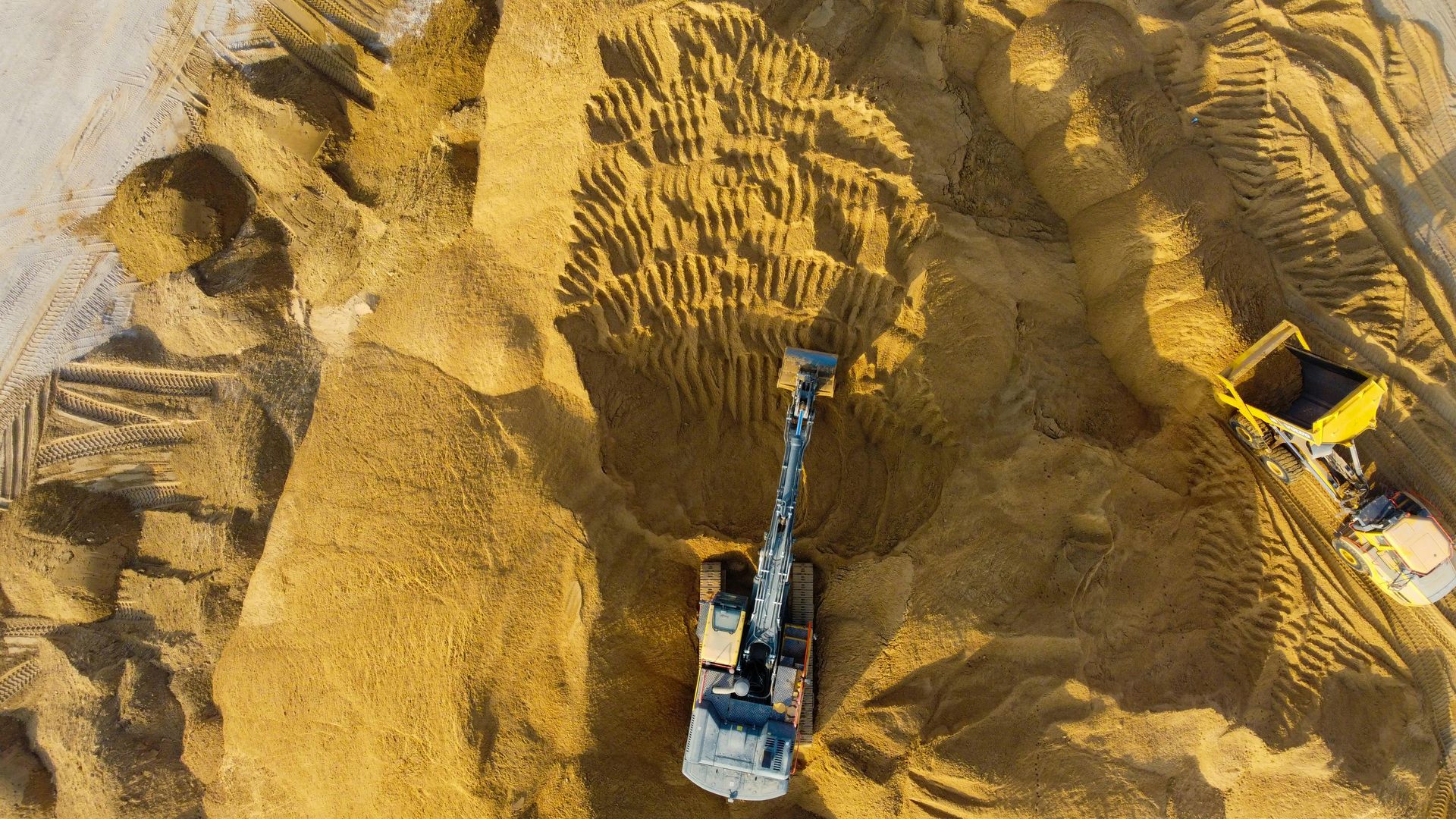 Bulldozer digging yellow sand at a quarry, with a truck nearby