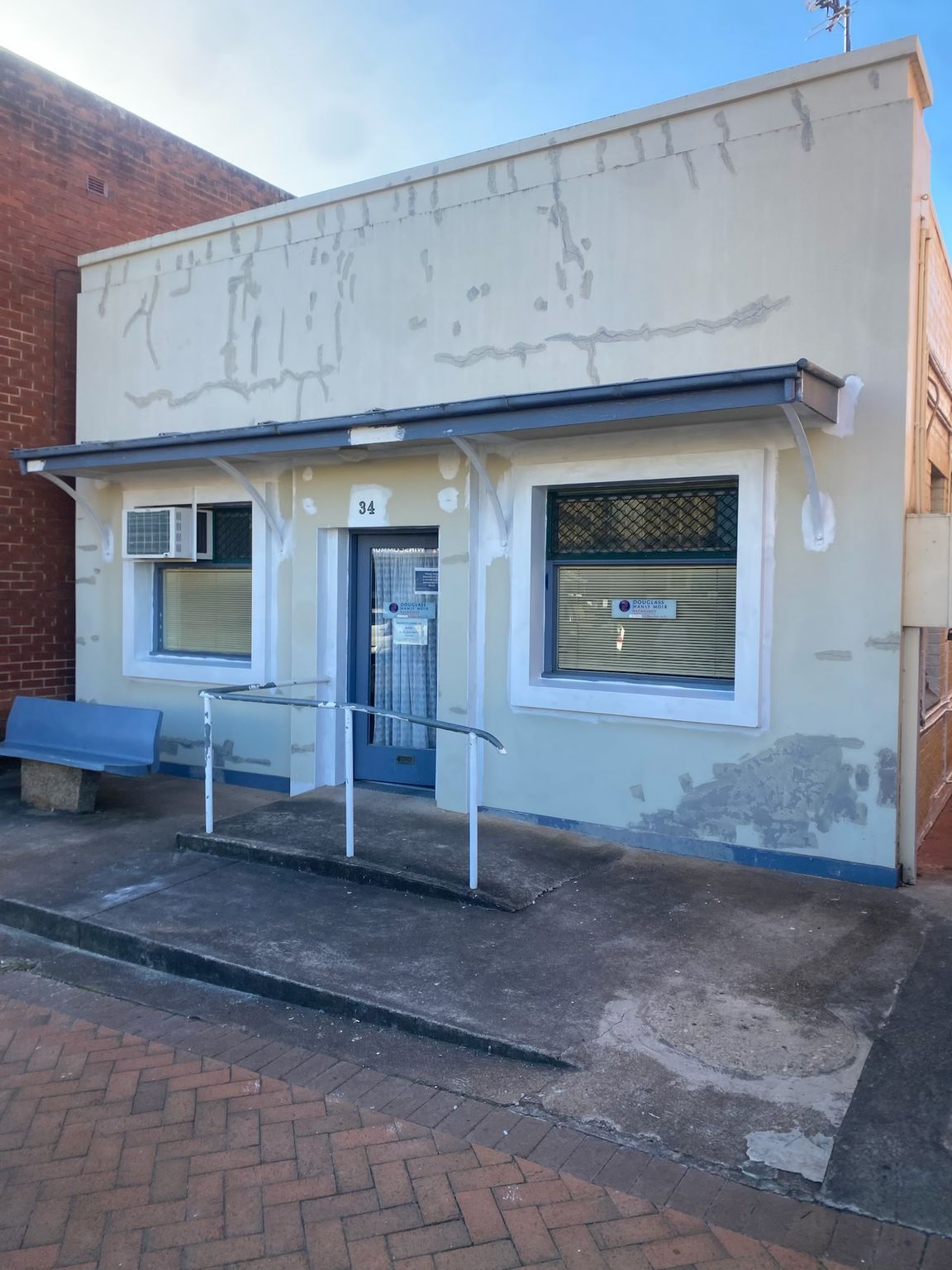Small white storefront with blue trim between red brick buildings on a wet brick street.