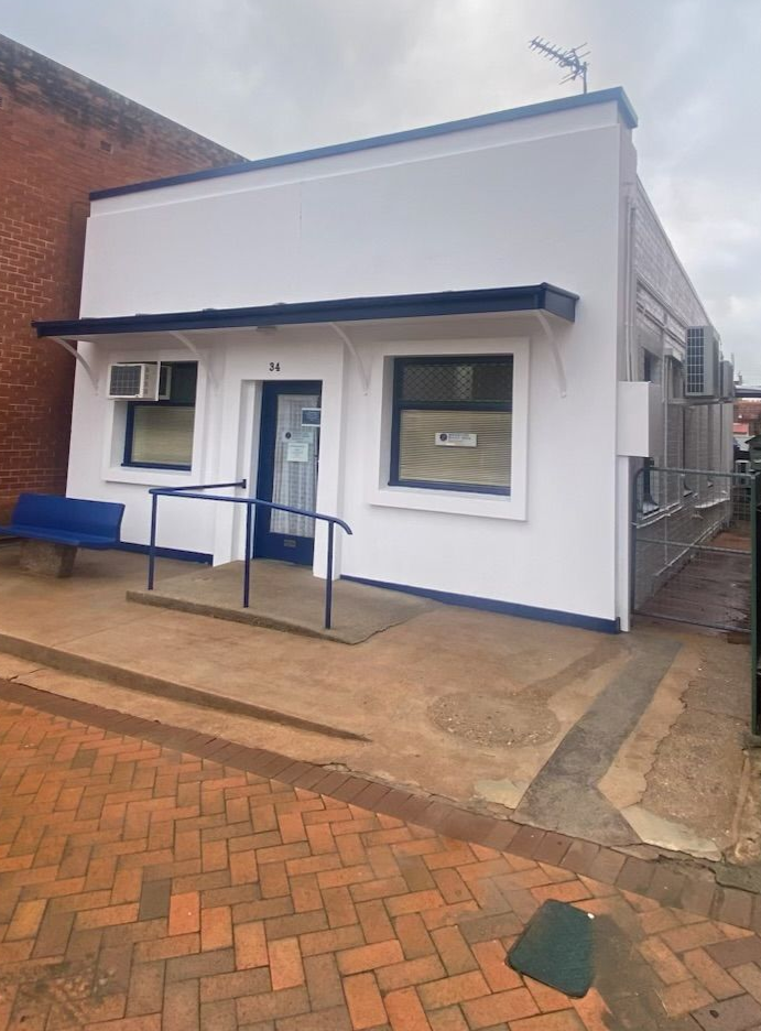 Small white building with blue trim, front windows, and a wheelchair ramp on a brick street — Robert Seeliger Painter And Decorator in Parkes, NSW