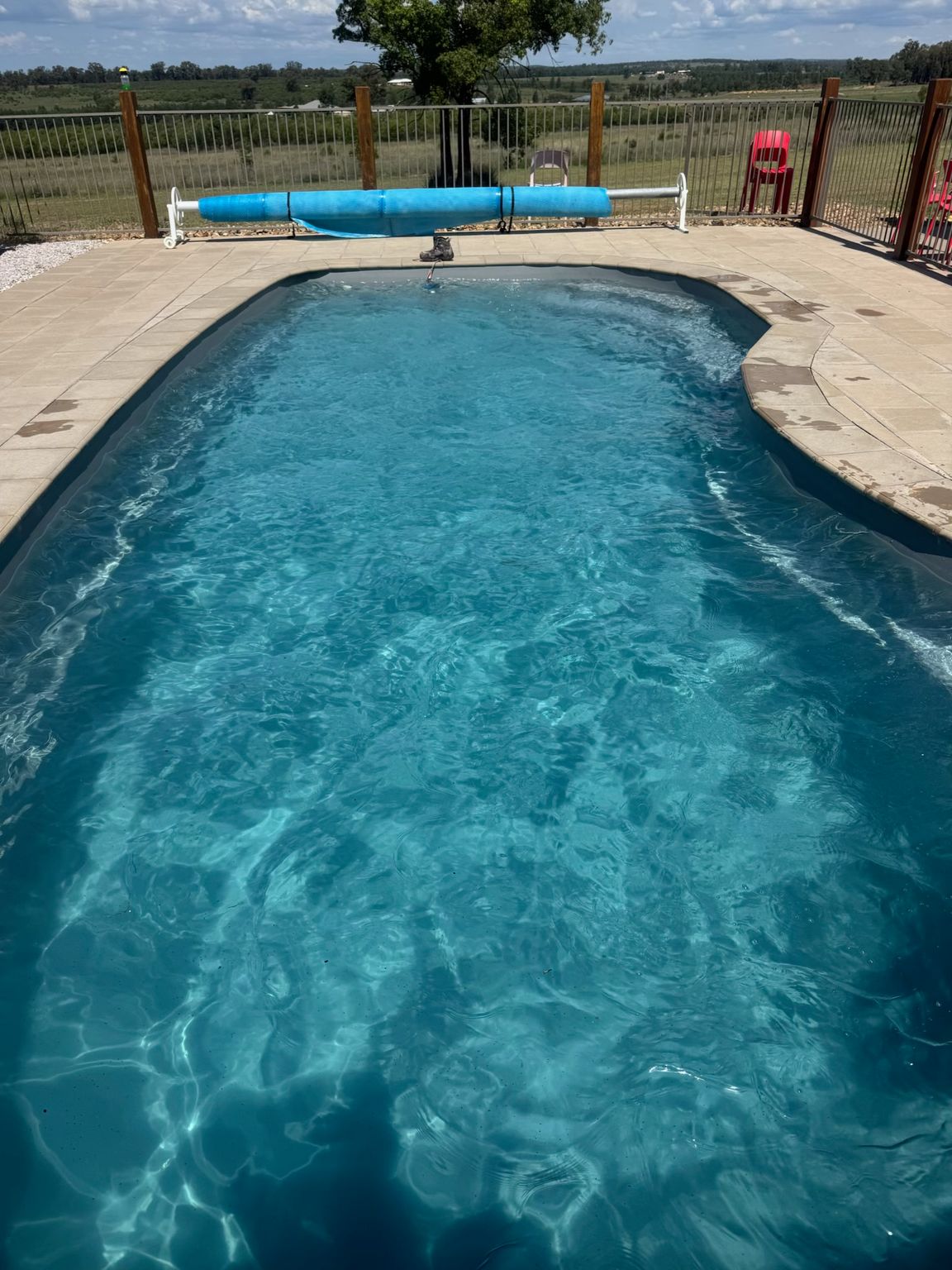 Backyard swimming pool with blue water, stone deck, and a fence overlooking open fields