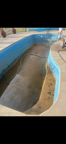 Empty drained swimming pool with blue-lined walls and a hose lying on the concrete bottom